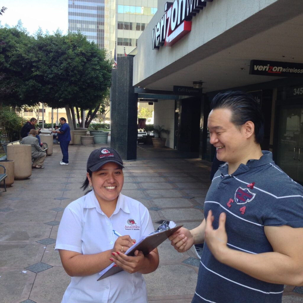 Analitika interviewer smiling as she records a respondent's answers on a clipboard, on a Los Angeles sidewalk