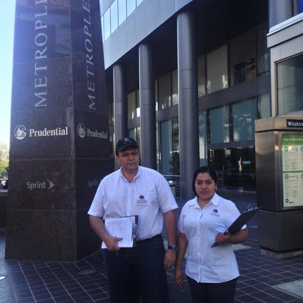 Two Analitika interviewers holding clipboards outside an office tower on Wilshire Boulevard