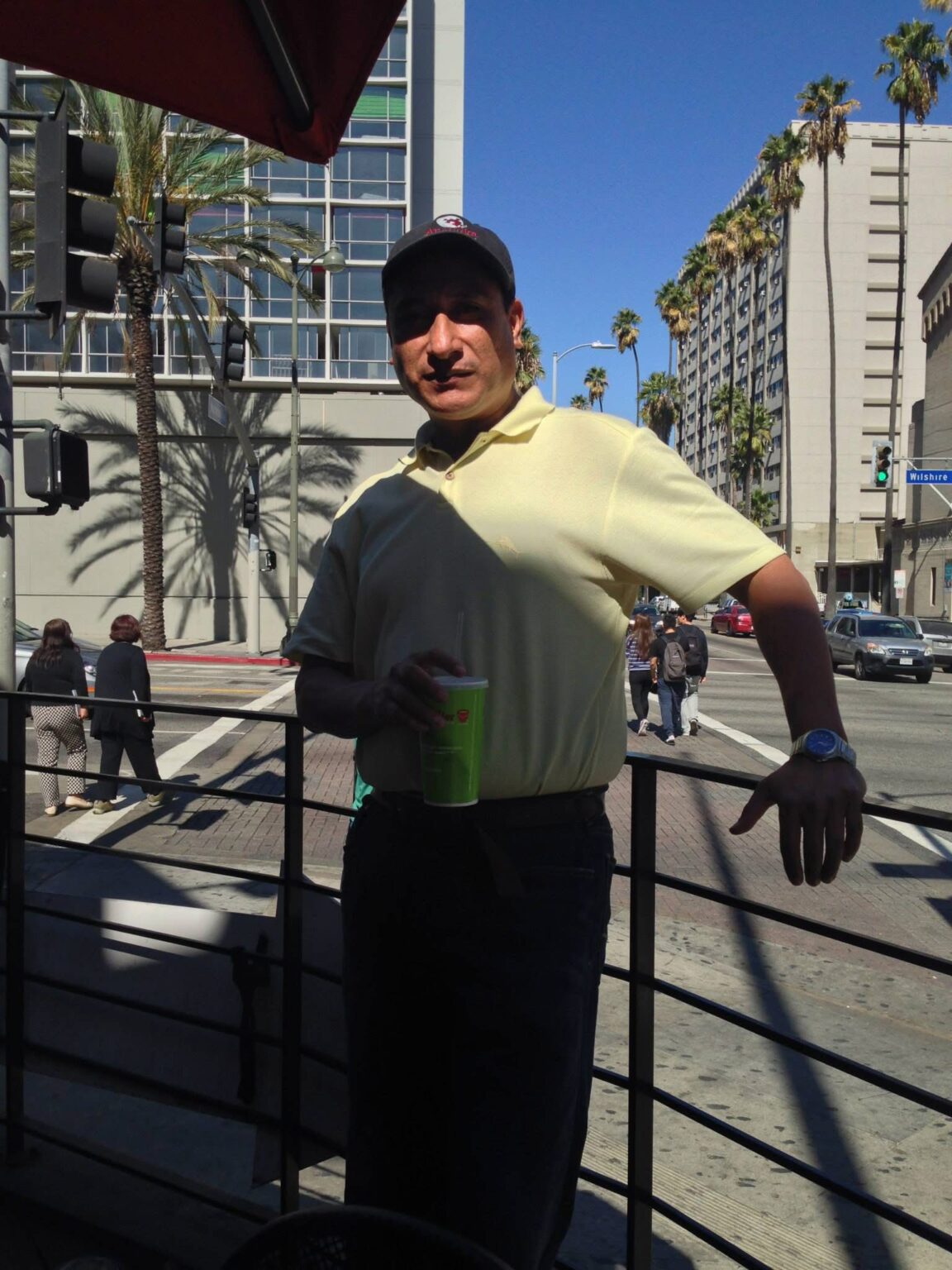 Analitika interviewer holding a drink at a Wilshire Boulevard intersection lined with palm trees