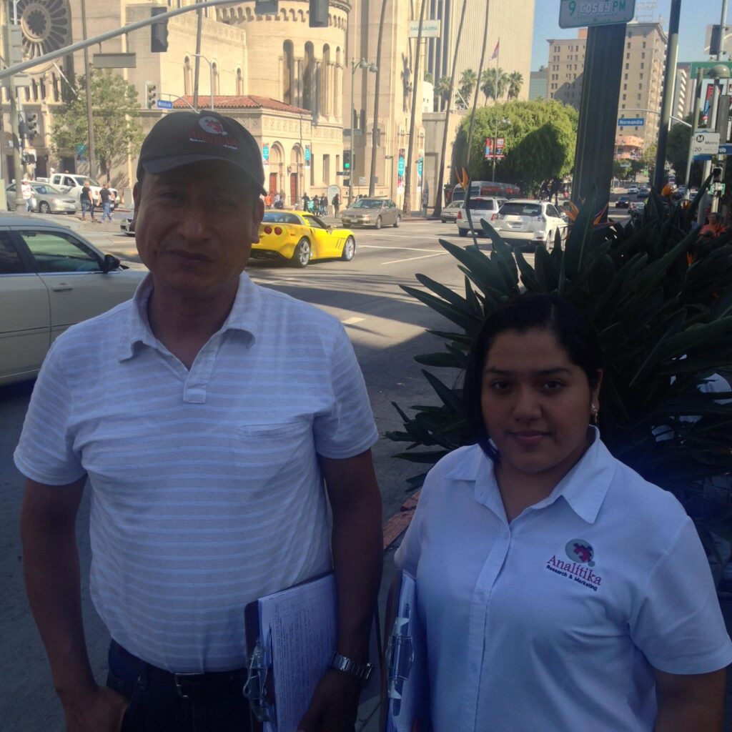 Two Analitika field interviewers with clipboards at the corner of Wilshire Boulevard and Normandie Avenue in Los Angeles