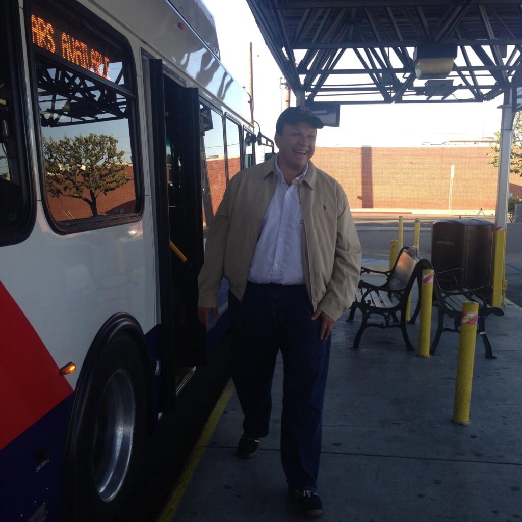 Smiling Analitika team member next to the open door of a city bus at a transit stop