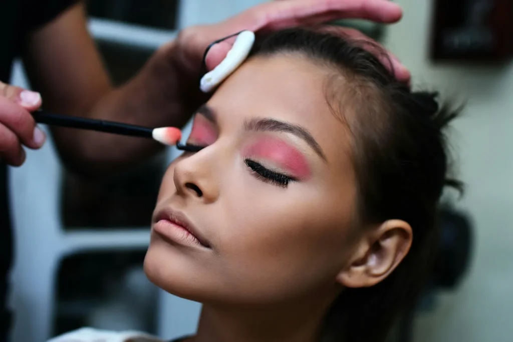 Maquillista aplica sombra de ojos rosada a una mujer