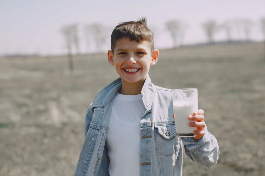 Niño sonriente sostiene un vaso de leche