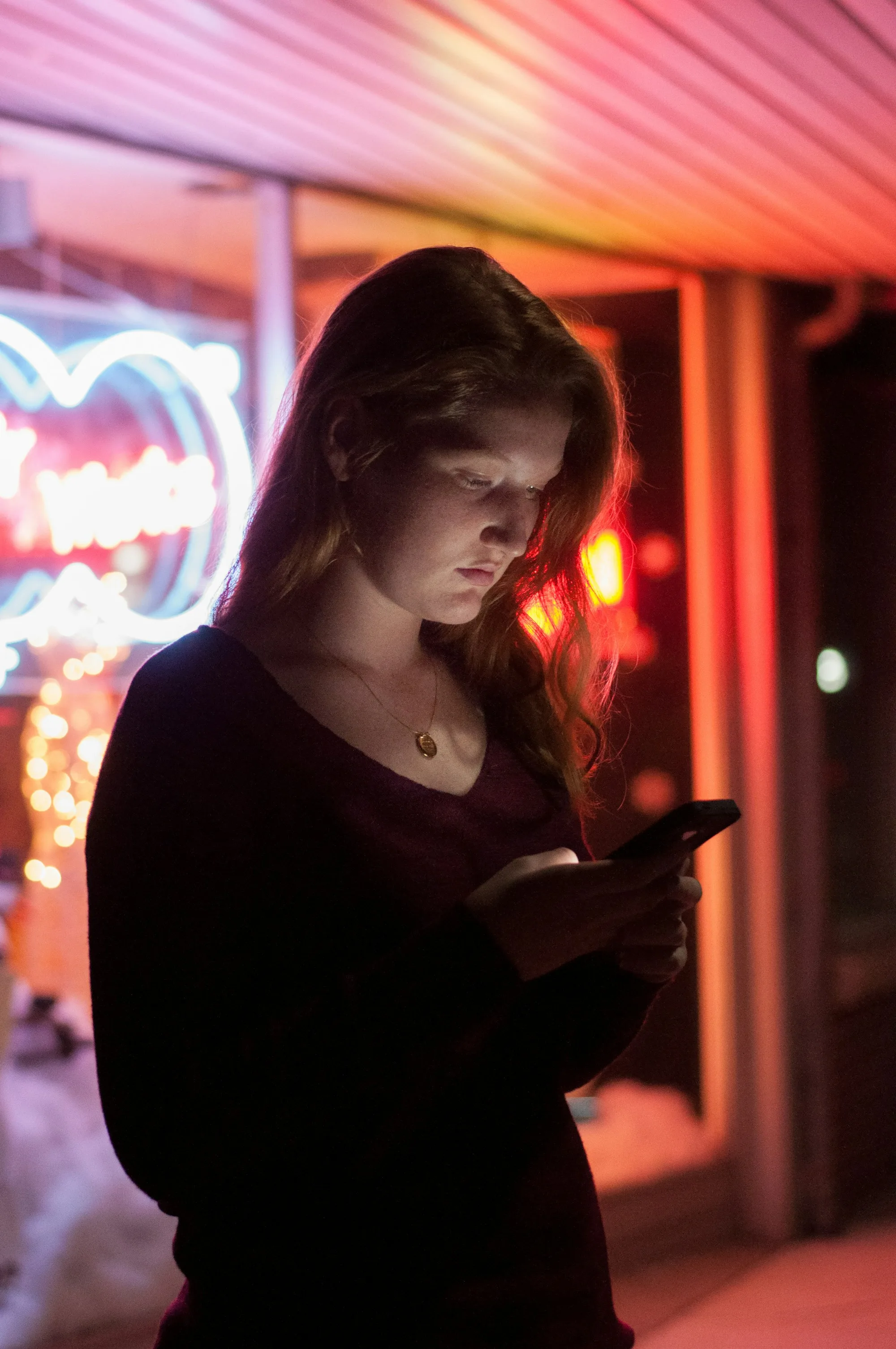 Joven revisa su celular de noche frente a un letrero luminoso